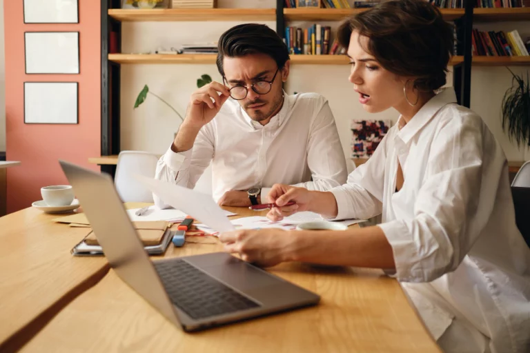 A man and woman collaborate on a laptop, focused on their work in a modern office setting