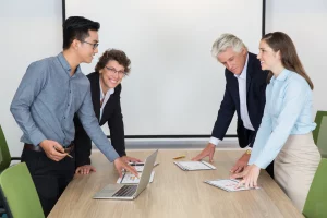 Three business professionals collaborating around a table, each with a laptop open in front of them.