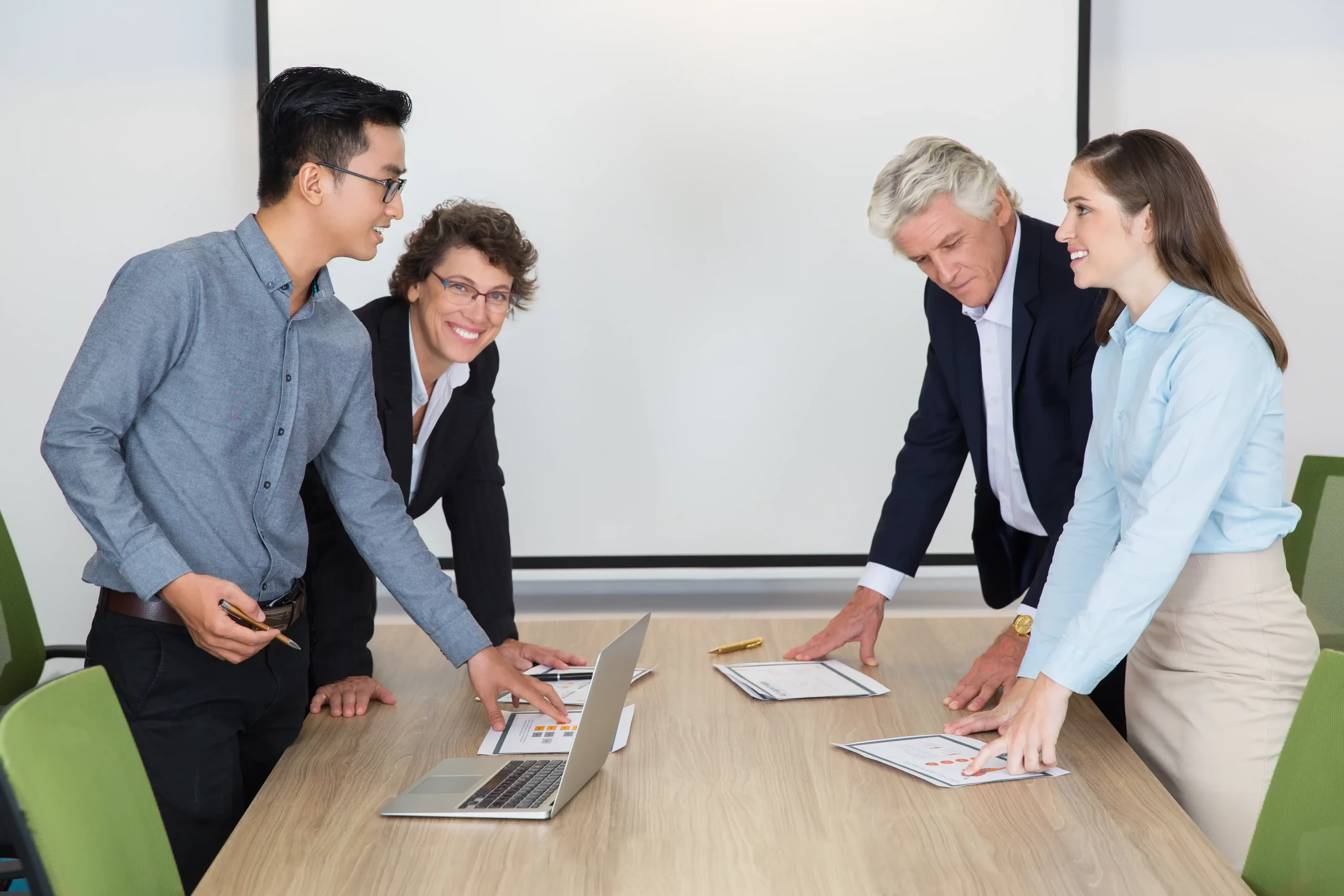 Three business professionals collaborating around a table, each with a laptop open in front of them.