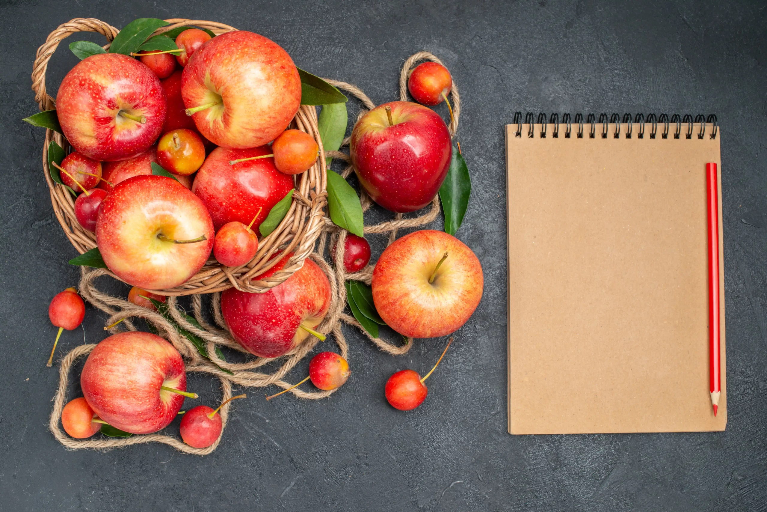 A red apple and a closed notebook resting on a black background, creating a simple yet striking composition.